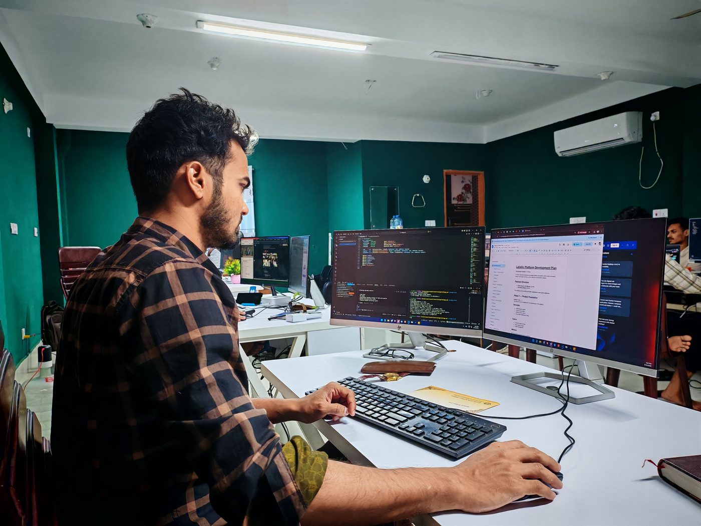 Desenvolvedor concentrado, trabalhando com código em múltiplos monitores em um escritório moderno.