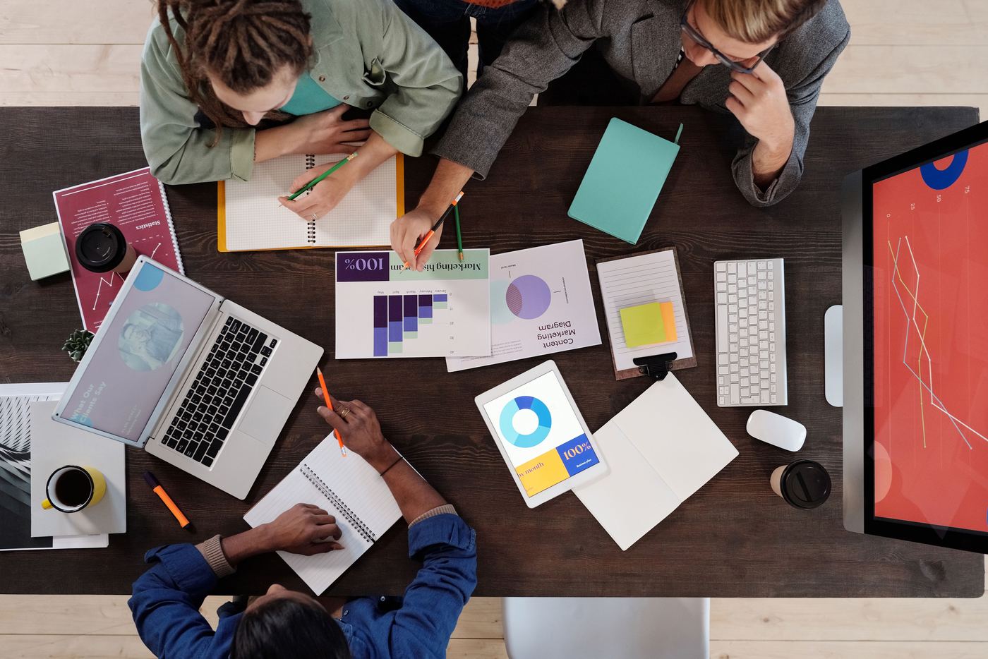 Equipe reunida em torno de uma mesa, colaborando em um projeto com notebooks e anotações.